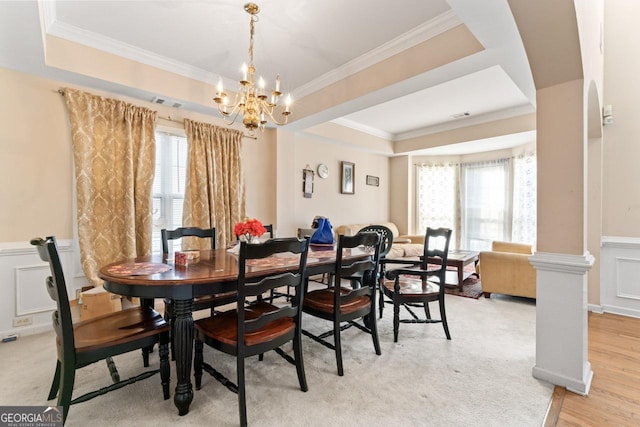 dining area with an inviting chandelier, a raised ceiling, ornamental molding, and light hardwood / wood-style floors