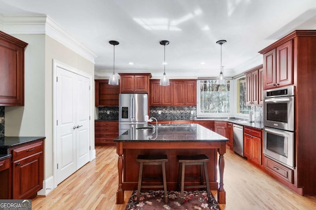 kitchen featuring pendant lighting, decorative backsplash, a center island with sink, appliances with stainless steel finishes, and ornamental molding