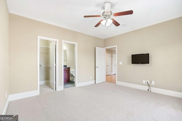 unfurnished bedroom with connected bathroom, a spacious closet, ceiling fan, light colored carpet, and ornamental molding