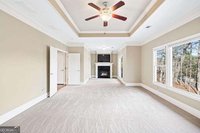 unfurnished living room featuring a tray ceiling, ceiling fan, crown molding, and light colored carpet