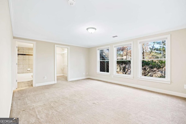 unfurnished bedroom featuring light carpet, ensuite bathroom, ornamental molding, a spacious closet, and a closet