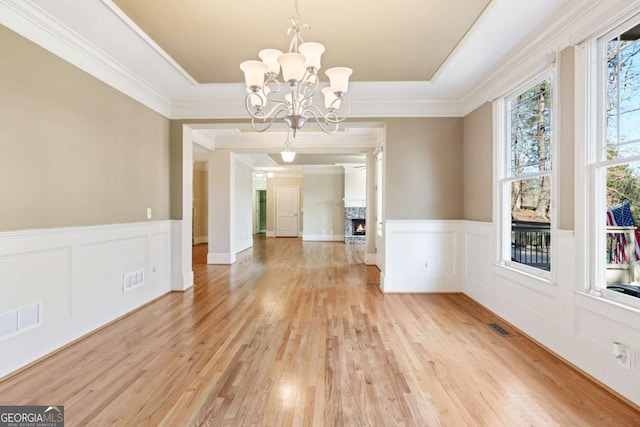 unfurnished dining area with a tray ceiling, a fireplace, a chandelier, and ornamental molding