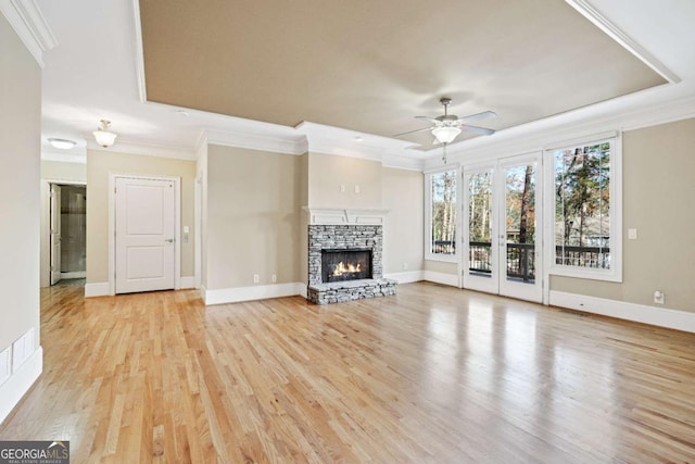 unfurnished living room with a stone fireplace, a raised ceiling, light hardwood / wood-style flooring, ceiling fan, and ornamental molding