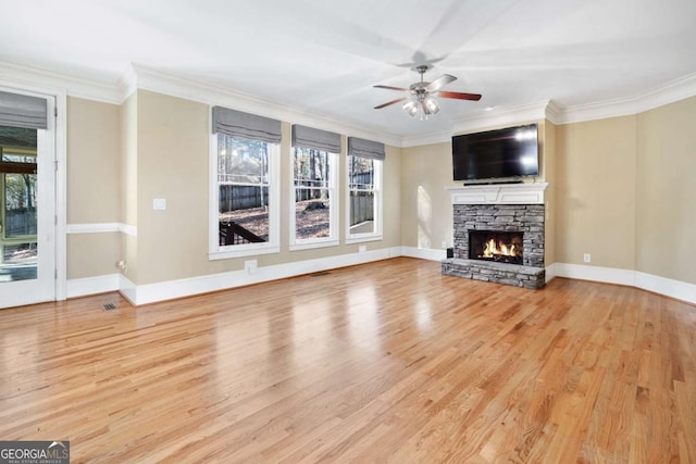 unfurnished living room with a stone fireplace, crown molding, ceiling fan, and light hardwood / wood-style floors