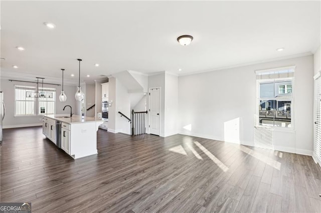 kitchen featuring sink, ornamental molding, an island with sink, decorative light fixtures, and white cabinetry