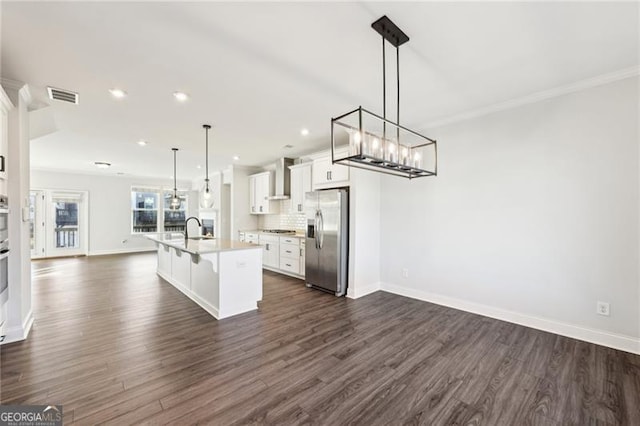 kitchen with white cabinetry, stainless steel appliances, an island with sink, decorative light fixtures, and a breakfast bar area