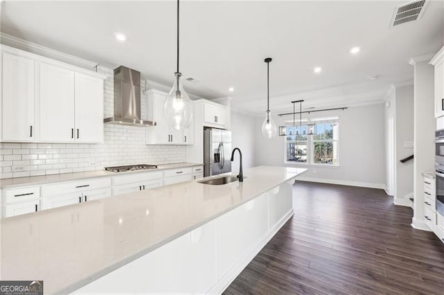 kitchen featuring wall chimney range hood, sink, hanging light fixtures, appliances with stainless steel finishes, and white cabinetry