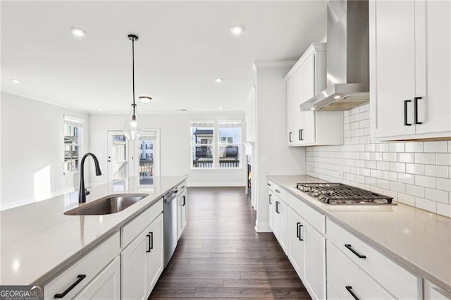 kitchen with stainless steel appliances, sink, wall chimney range hood, decorative light fixtures, and white cabinets