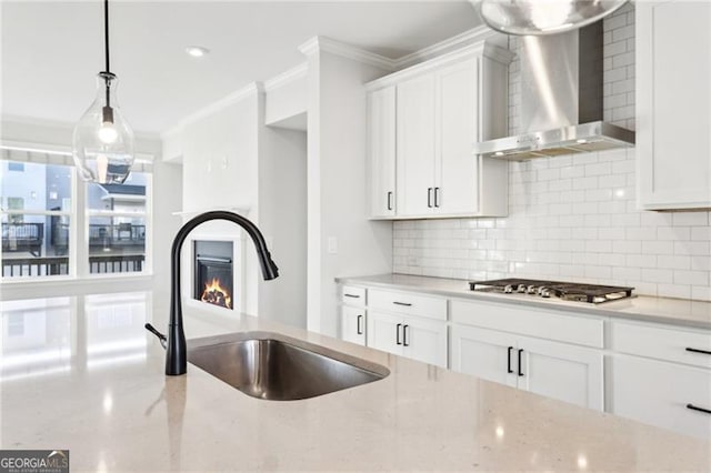 kitchen featuring sink, wall chimney range hood, decorative light fixtures, white cabinetry, and stainless steel gas stovetop