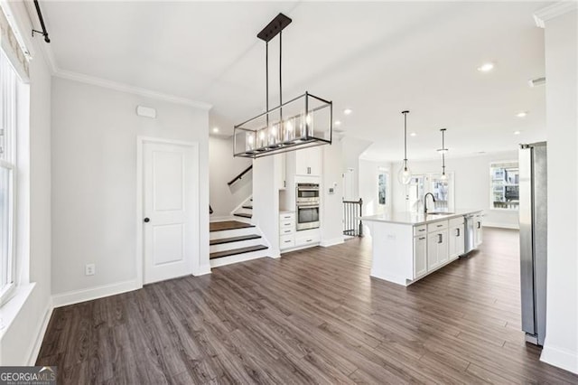 kitchen with dark wood-type flooring, sink, a center island with sink, white cabinetry, and hanging light fixtures