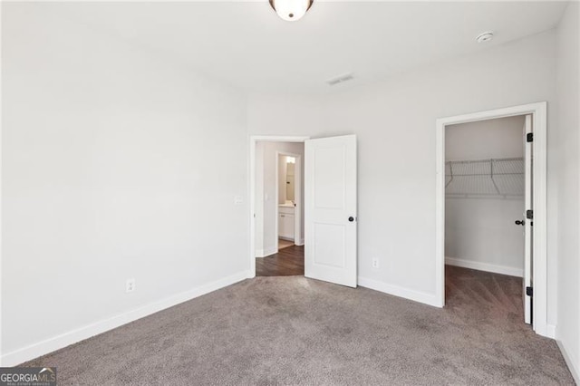 unfurnished bedroom featuring dark colored carpet, a spacious closet, and a closet