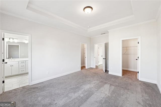 unfurnished bedroom featuring a walk in closet, a tray ceiling, light colored carpet, connected bathroom, and a closet