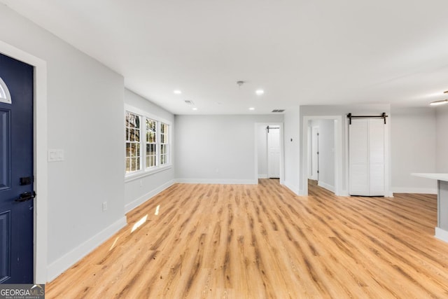 unfurnished living room featuring a barn door and light hardwood / wood-style flooring