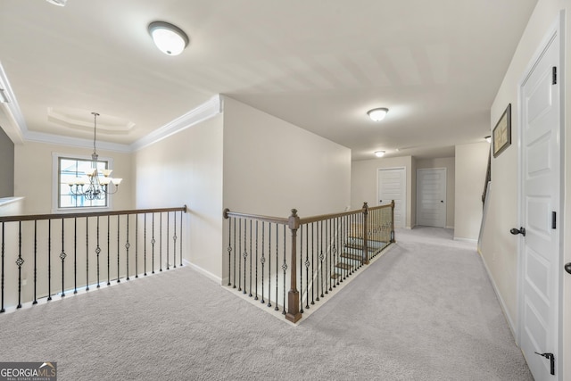 hallway with a raised ceiling, light carpet, ornamental molding, and a notable chandelier