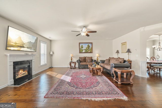 living room featuring ceiling fan with notable chandelier and dark wood-type flooring