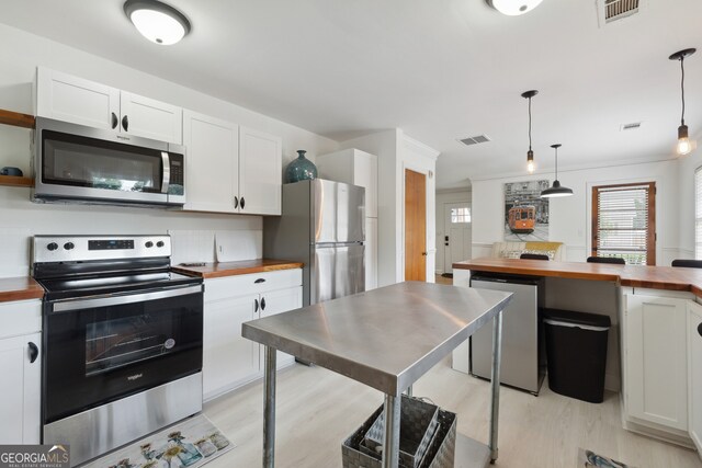 kitchen with pendant lighting, wooden counters, white cabinets, and stainless steel appliances