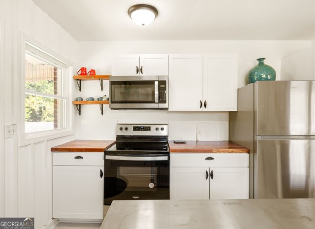 kitchen with appliances with stainless steel finishes, white cabinetry, and butcher block counters