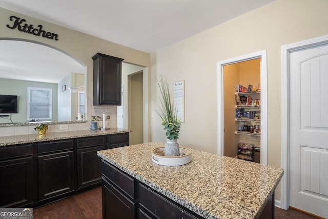 kitchen featuring backsplash, light stone countertops, dark hardwood / wood-style flooring, and a kitchen island