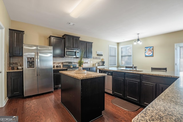 kitchen featuring light stone countertops, sink, a center island, hanging light fixtures, and stainless steel appliances