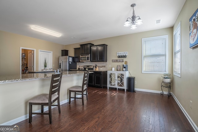 kitchen with a kitchen breakfast bar, light stone counters, stainless steel appliances, decorative light fixtures, and an inviting chandelier