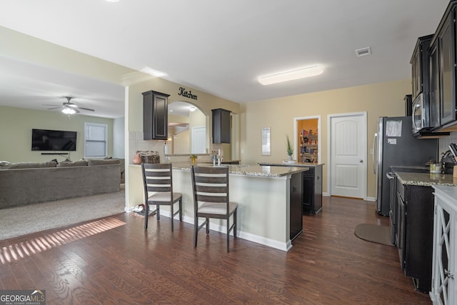 kitchen with a kitchen bar, dark hardwood / wood-style flooring, light stone counters, and ceiling fan