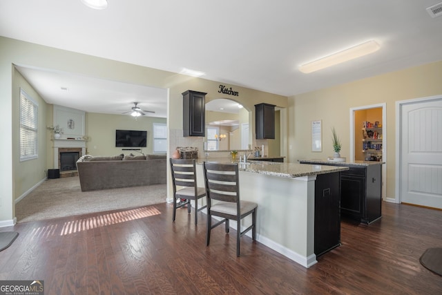 kitchen featuring a breakfast bar, ceiling fan, dark hardwood / wood-style floors, a kitchen island, and light stone counters