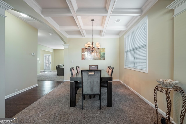 carpeted dining room with ornate columns, coffered ceiling, crown molding, beam ceiling, and a chandelier