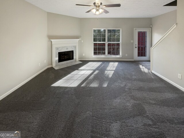 unfurnished living room featuring a high end fireplace, a textured ceiling, ceiling fan, and dark colored carpet