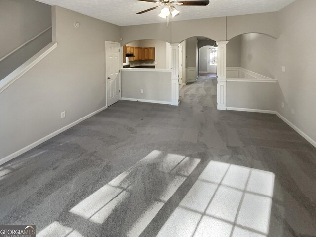 unfurnished living room with a textured ceiling, dark carpet, ceiling fan, and ornate columns