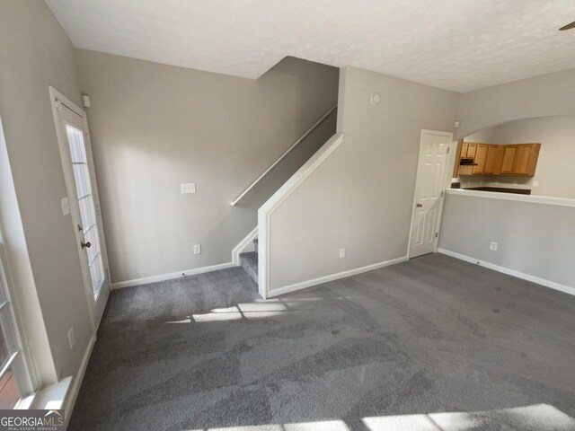 unfurnished living room with dark colored carpet and a textured ceiling