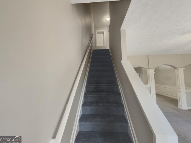 stairway with carpet floors, a textured ceiling, and decorative columns