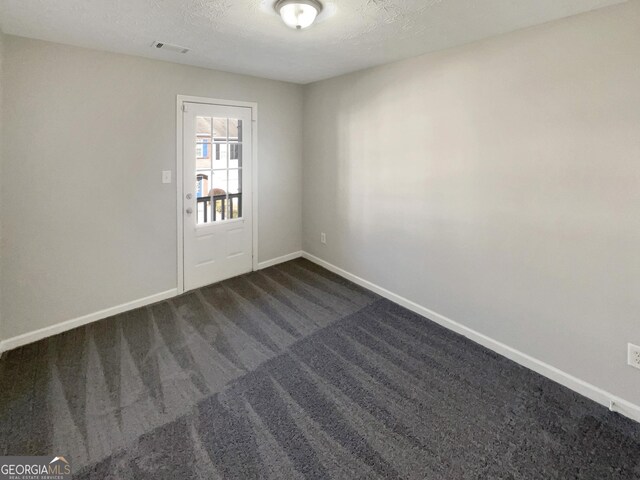 spare room with dark colored carpet and a textured ceiling