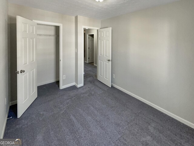 unfurnished bedroom with dark colored carpet, a textured ceiling, and a closet