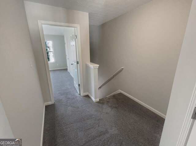 corridor featuring dark carpet and a textured ceiling