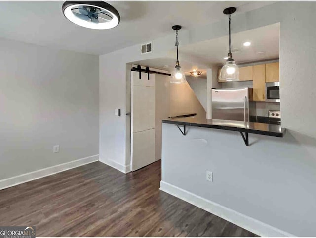 kitchen with a breakfast bar, hanging light fixtures, a barn door, kitchen peninsula, and stainless steel appliances