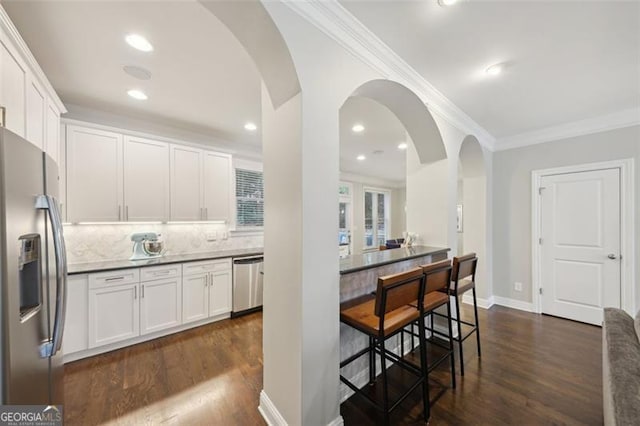 kitchen with tasteful backsplash, ornamental molding, stainless steel appliances, white cabinets, and dark hardwood / wood-style floors