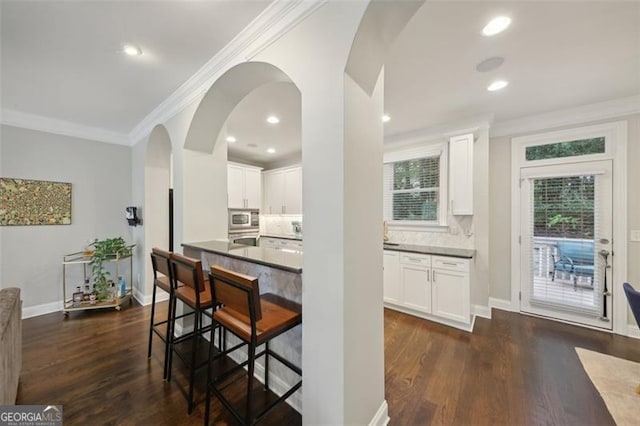 kitchen with a kitchen breakfast bar, decorative backsplash, white cabinetry, and stainless steel microwave