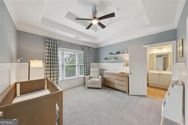 bedroom featuring light carpet, ensuite bathroom, ornamental molding, a raised ceiling, and ceiling fan