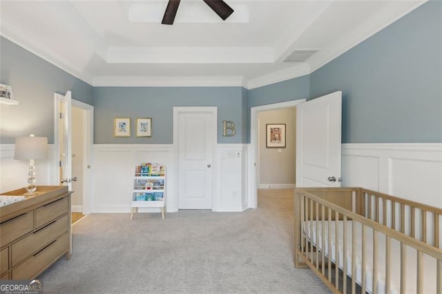 carpeted bedroom with a crib, a raised ceiling, ceiling fan, and ornamental molding