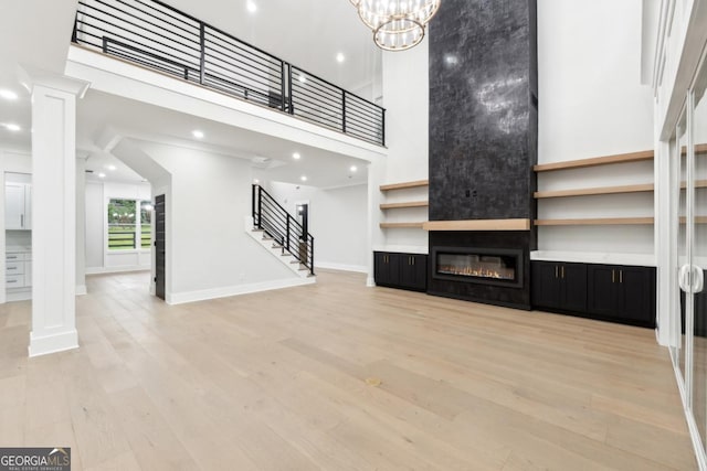 unfurnished living room with a large fireplace, ornate columns, a high ceiling, and light hardwood / wood-style flooring