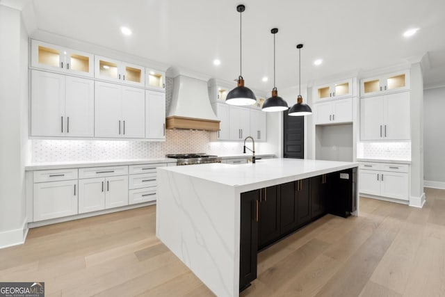 kitchen with white cabinets, pendant lighting, a center island with sink, and custom exhaust hood