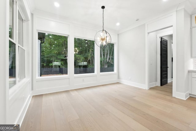 unfurnished dining area featuring crown molding, a chandelier, and light wood-type flooring