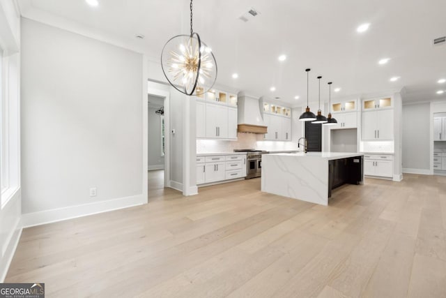 kitchen featuring tasteful backsplash, premium range hood, high end stove, a kitchen island with sink, and white cabinetry