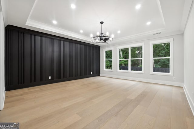 empty room with an inviting chandelier, light wood-type flooring, crown molding, and a tray ceiling