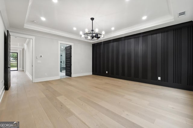 spare room featuring a raised ceiling, crown molding, a chandelier, and light hardwood / wood-style floors