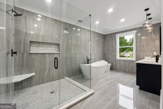 bathroom featuring separate shower and tub, vanity, and tile walls