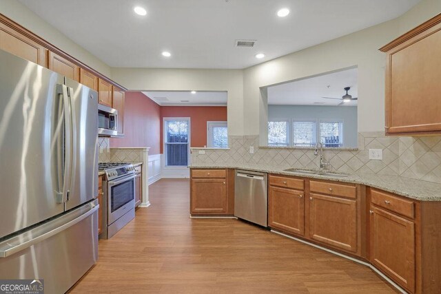 kitchen featuring ceiling fan, sink, light stone counters, appliances with stainless steel finishes, and light wood-type flooring