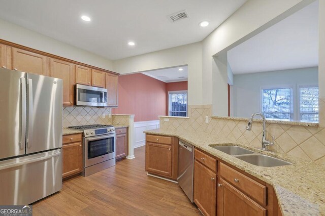 kitchen featuring light stone counters, sink, stainless steel appliances, and light hardwood / wood-style flooring