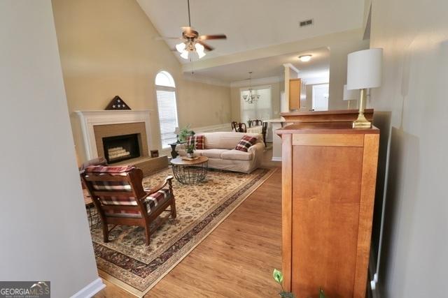 living room with hardwood / wood-style flooring, ceiling fan with notable chandelier, and vaulted ceiling