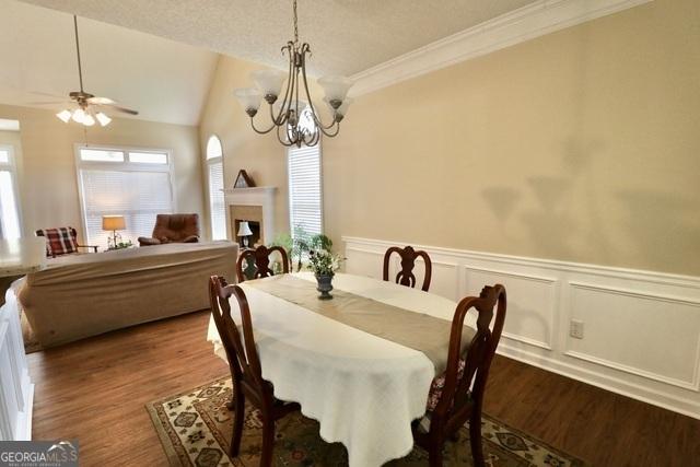 dining area with crown molding, a textured ceiling, lofted ceiling, ceiling fan with notable chandelier, and hardwood / wood-style flooring